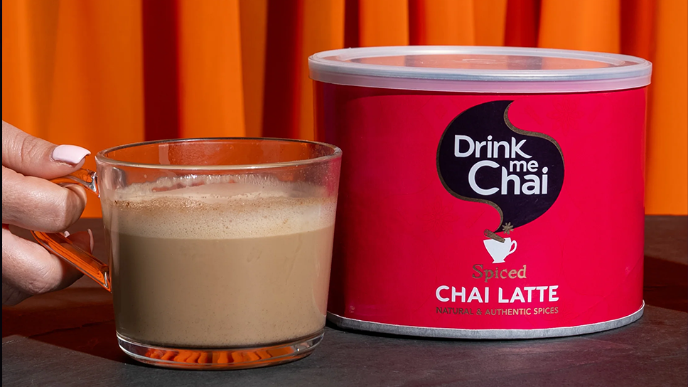 drink me chai spiced chai 1kg tin with made cup next to pack 