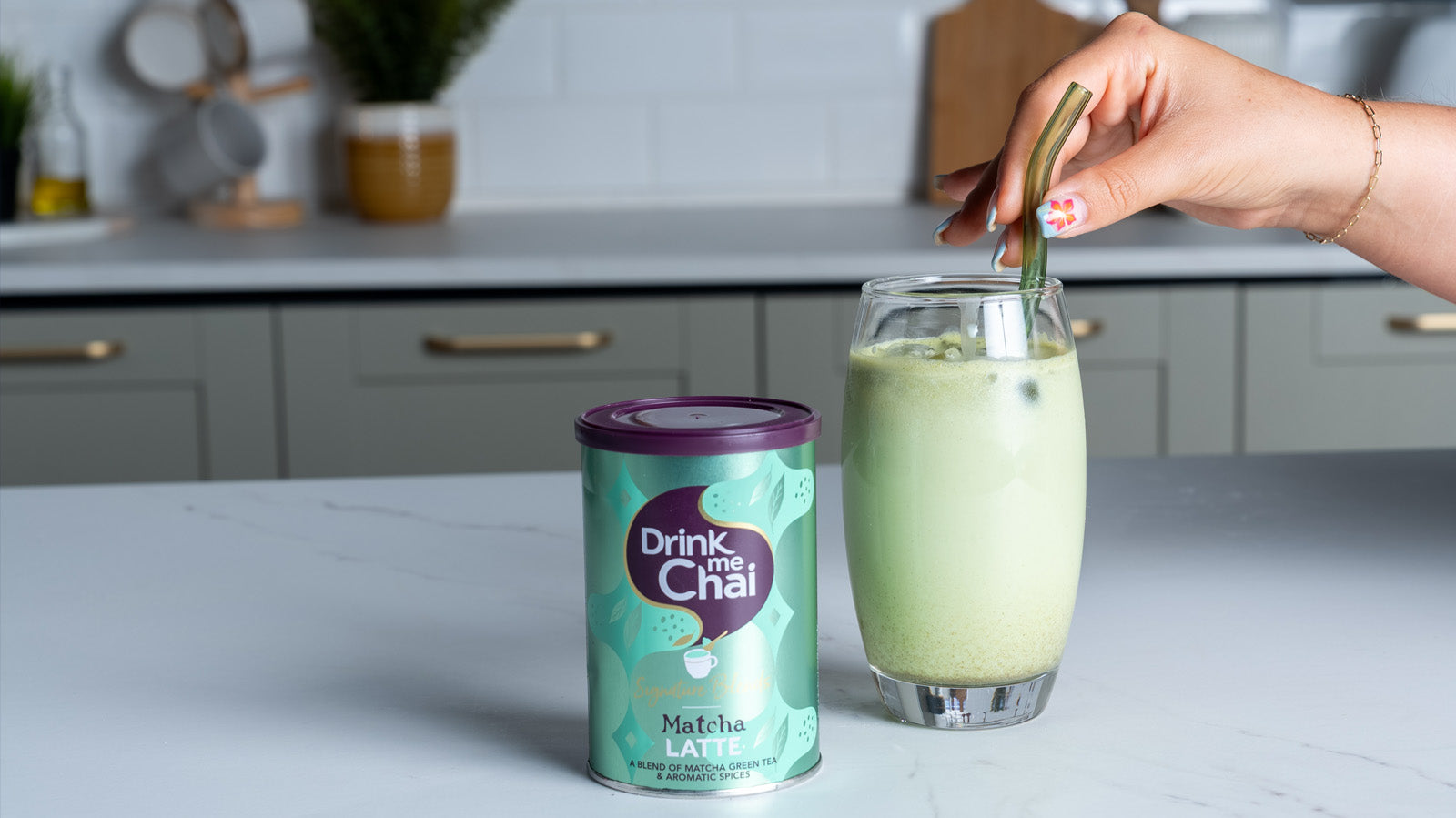 Drink me Chai Matcha Latte packshot next to made matcha latte in glass with straw