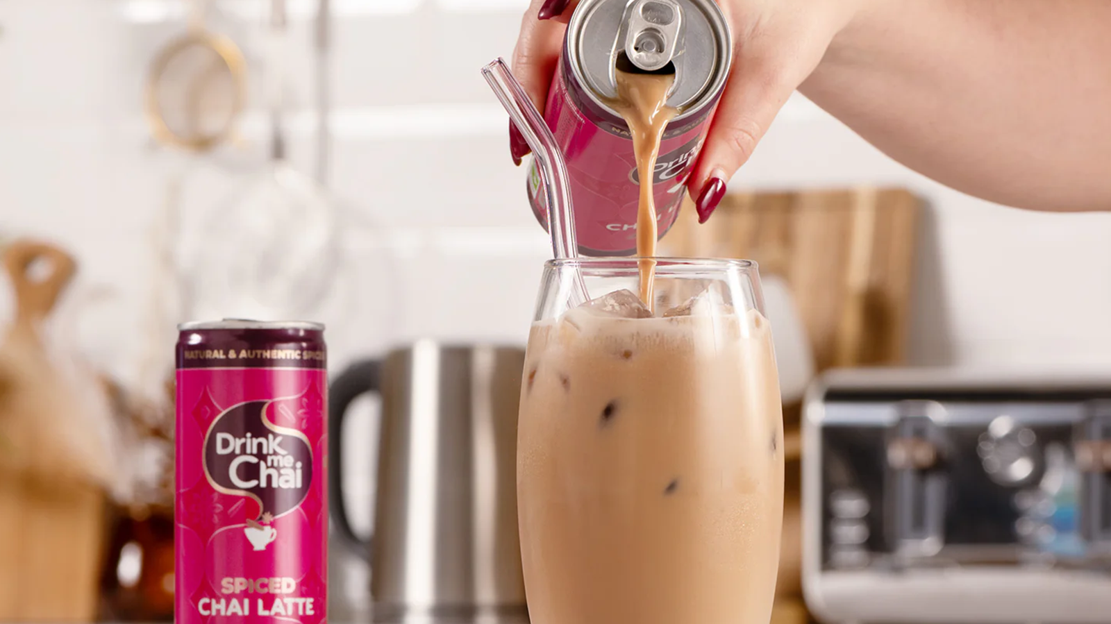 female hand pouring a ready to drink chai can into a glass with straw on kitchen worktop
